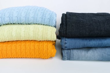 Katlanmış renkli kazak yığını, mavi kot pantolonlu kazak beyaz arka plana yakın.