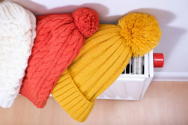 Colorful winter knitted caps, hats hanging and drying on a hot central heating radiator, winter family outdoor activities and sports concept — Stock Photo, Image