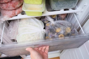 Dondurucunun çekmecesini açan bir el. Donmuş gıdalar, uzun vadeli yiyecek depolama ve evde stoklar.