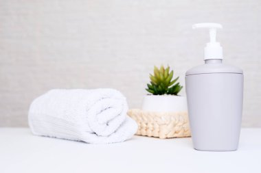 Pastel renkler, gri sabun makinesi, beyaz havlu ve kaplıca, vücut ve yüz bakımı için saksı bitkisi.