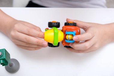Beyaz bir masada oyuncak araba oynayan bir çocuk.