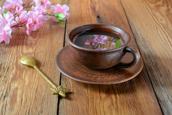 Eine Tasse Tee mit einem Spiegelbild eines Kirschzweiges auf einem dunkel strukturierten Holztisch. Selektiver Fokus. Das Konzept der Erholung. — Stockfoto