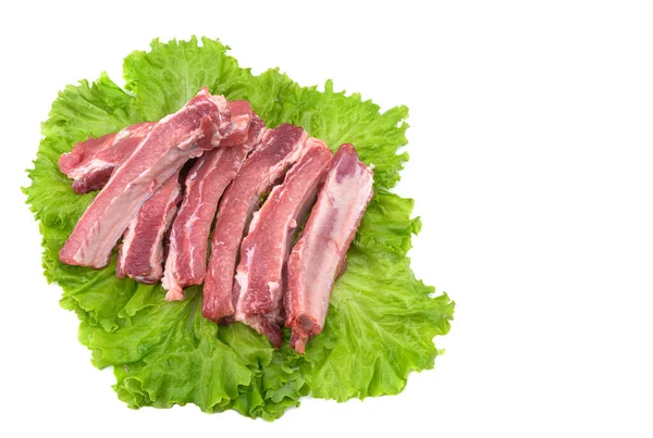 Las costillas de cerdo crudas sobre una hoja de lechuga están aisladas sobre un fondo blanco. — Foto de Stock