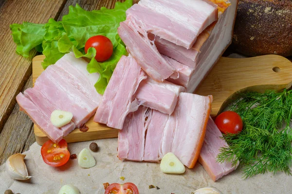 Geräucherter Schweinebauch in Scheiben, Speck, Schinken mit Kräutern, Tomaten und schwarzem Pfeffer auf Lebensmittelpapier. Holz rustikaler Hintergrund. Selektiver Fokus. — Stockfoto