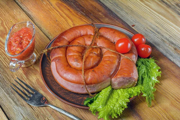 Wędzona kiełbasa, skręcona w spirali w talerzu ziół na starym drewnianym stole rustykalnym.Żywność domowej roboty.. — Zdjęcie stockowe