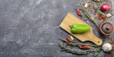Sarımsak, biberiye, defne yaprakları, biber, soğan ve aromatik mevsimlerle birlikte ahşap kesim tahtasıyla birlikte koyu bir mutfak arka planı var..