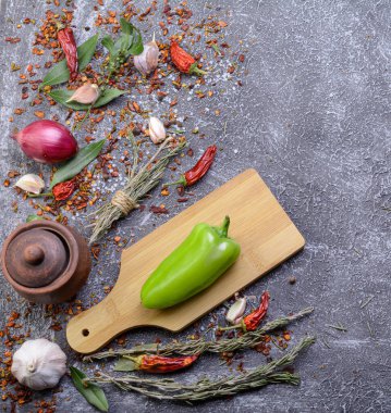 Sarımsak, biberiye, defne yaprakları, biber, soğan ve aromatik mevsimlerle birlikte ahşap kesim tahtasıyla birlikte koyu bir mutfak arka planı var..