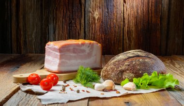 Tütsülenmiş domuz eti, domuz pastırması, otlu jambon, domates ve kağıt üzerinde karabiber. Ahşap kırsal arka plan. Seçmeli odak noktası. Yatay görüş.