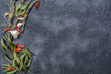 Sarımsak, biberiye, defne yaprakları, biber, soğan ve aromatik mevsimlerle birlikte ahşap kesim tahtasıyla birlikte koyu bir mutfak arka planı var..