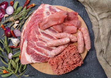 Çeşit çeşit et. Çiğ domuz kaburgası, kıyma, sosis ve karbonatı yuvarlak bir kesim tahtasına yerleştir. Et tabağı pişirme mevsimleri. Seçici odak, üst görünüm.