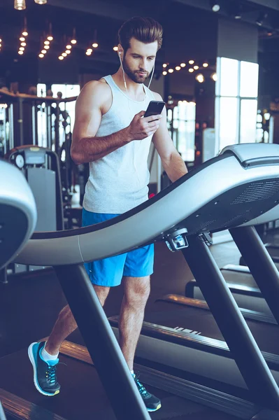 英俊的男人在跑步机上用手机上 — 图库照片