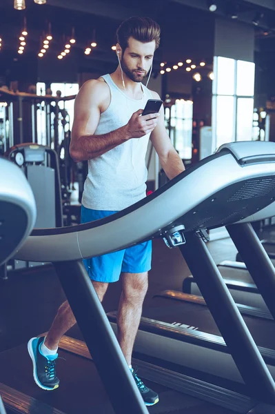 Bell'uomo sul tapis roulant con telefono — Foto Stock