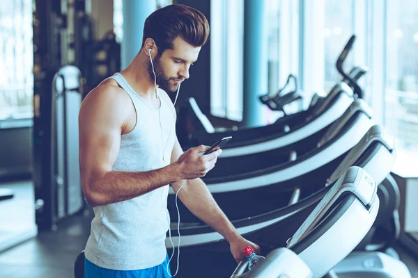 Bell'uomo con telefono sul tapis roulant — Foto Stock