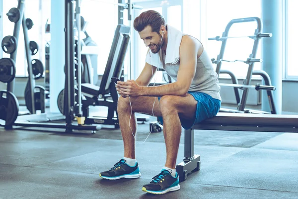 Junger Mann mit Kopfhörer und Handy im Fitnessstudio — Stockfoto