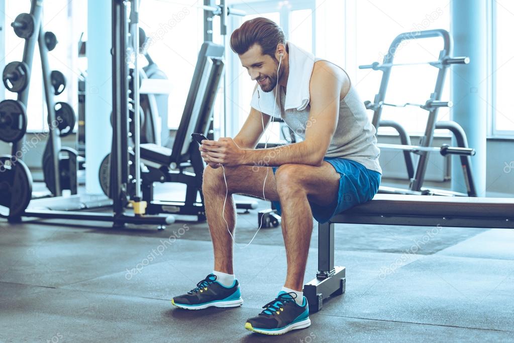 young man in headphones with phone at gym