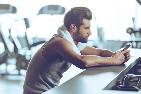 Joven usando el teléfono en el gimnasio — Foto de Stock