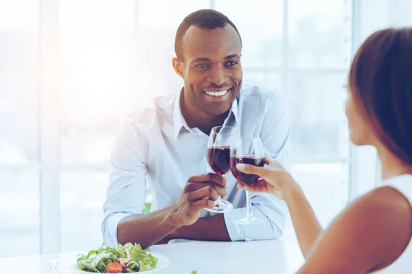 Cena romántica.. Hermosa pareja africana joven sentados juntos en la mesa y sosteniendo las gafas de vino — Foto de Stock
