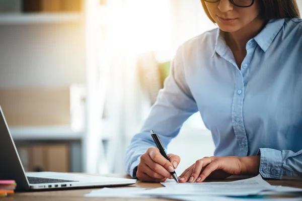 Firmare nuovi contratti. Parte di primo piano della giovane donna che firma documenti mentre è seduta sul posto di lavoro — Foto Stock