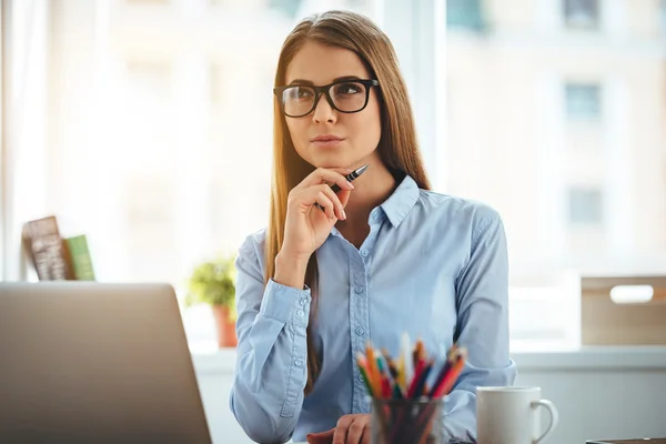New day new decisions. Pensive young beautiful woman holding hand on chin and looking thoughtful while sitting at her working place — Stock Photo, Image