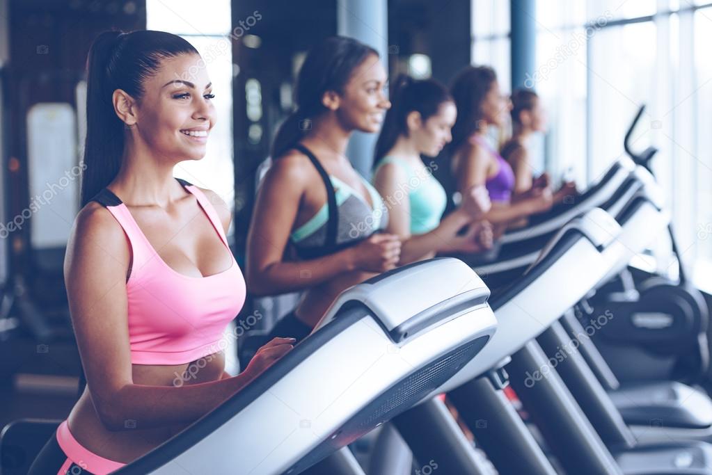 Beautiful women running on treadmill at gym Stock Photo by