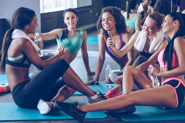 Hermosas mujeres jóvenes sentadas en la alfombra de ejercicio en el gimnasio — Foto de Stock