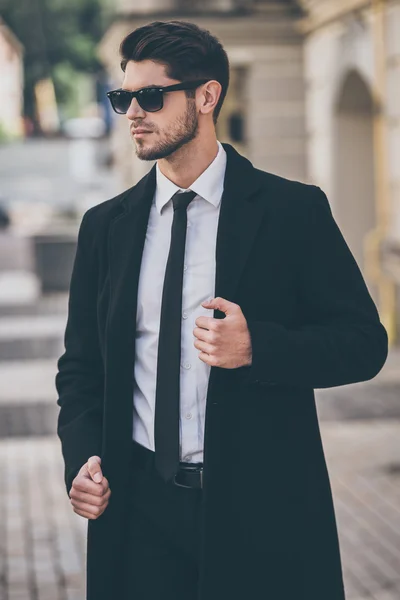 Человек в солнцезащитных очках регулирует свое пальто — стоковое фото