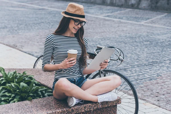 Женщина смотрит на свой цифровой планшет и держа чашку кофе — стоковое фото