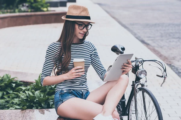 woman looking at her digital tablet and drinking coffee