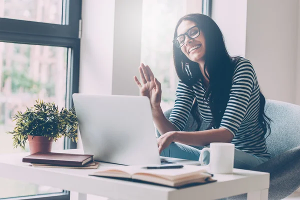 Woman waving while looking at her laptop — Stockfoto