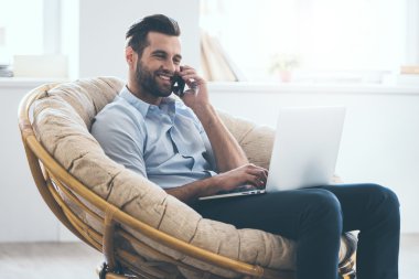 adam dizüstü bilgisayar üzerinde çalışıyor ve telefonda konuşurken
