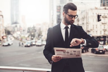 gazete tutan ve saatine bakan adam