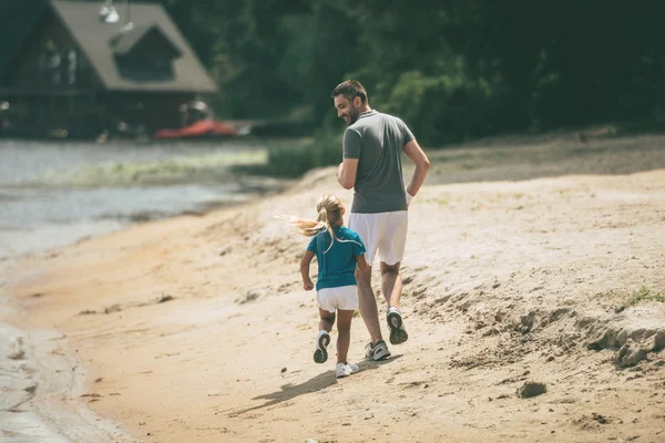 Padre e hija corriendo en la orilla del río — Foto de Stock