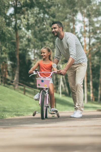 Отец учит свою дочь кататься на велосипеде — стоковое фото