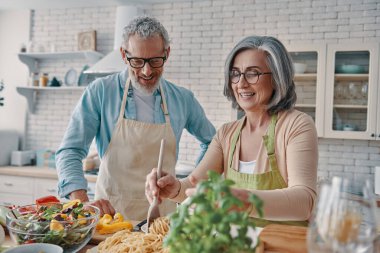 Beautiful senior couple in aprons preparing healthy dinner and smiling while spending time at home