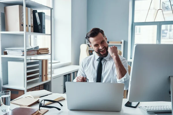 Stock image Cheerful young man in shirt and tie working using computer and smiling while sitting in the office