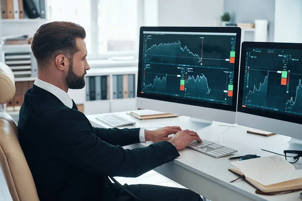 Jeune homme concentré en chemise et cravate analysant les données sur le marché boursier tout en travaillant au bureau — Photo