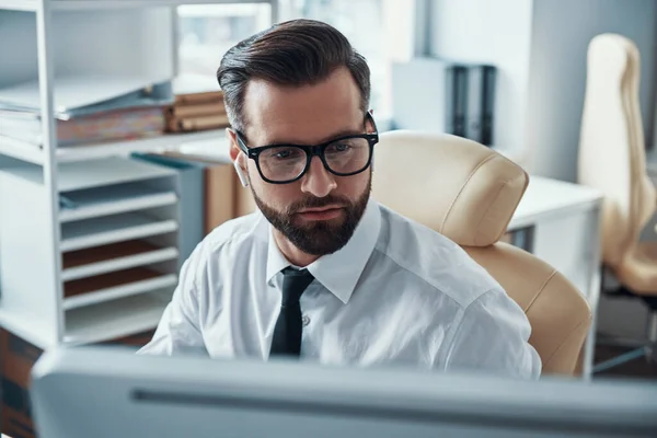 Geconcentreerde jonge man in shirt en stropdas werken op de computer tijdens het zitten in het kantoor — Stockfoto