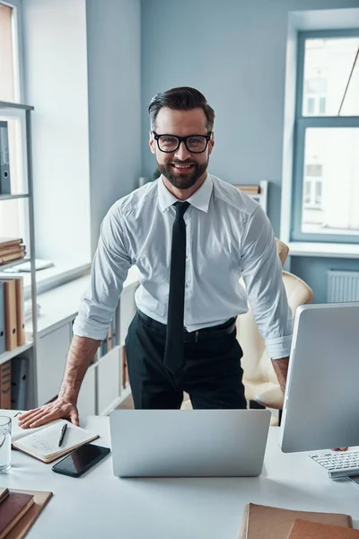 Stilig ung man i formalwear tittar på kameran och ler medan du arbetar på kontoret — Stockfoto