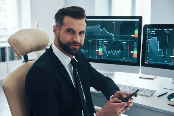 Handsome young man in shirt and tie looking at camera and smiling while working in the office — Stock Photo, Image