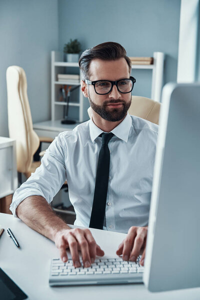 Modern young man in formalwear working on computer while sitting in the office