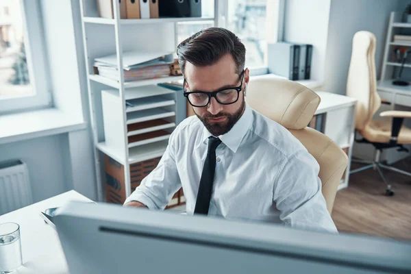 Gömlekli ve kravatlı modern genç adam ofiste otururken teknoloji kullanarak çalışıyor. — Stok fotoğraf
