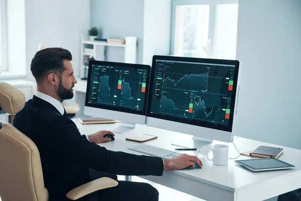 Seriöser junger Mann in Hemd und Krawatte, der im Büro Daten über den Aktienmarkt analysiert — Stockfoto