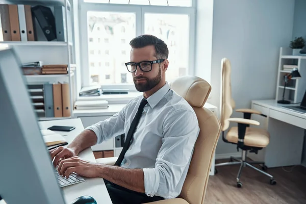 Jovem homem inteligente em formalwear trabalhando no computador enquanto sentado no escritório — Fotografia de Stock