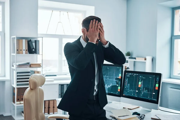 Stressad ung man i formalwear täcker ansiktet med händerna medan du arbetar på kontoret — Stockfoto