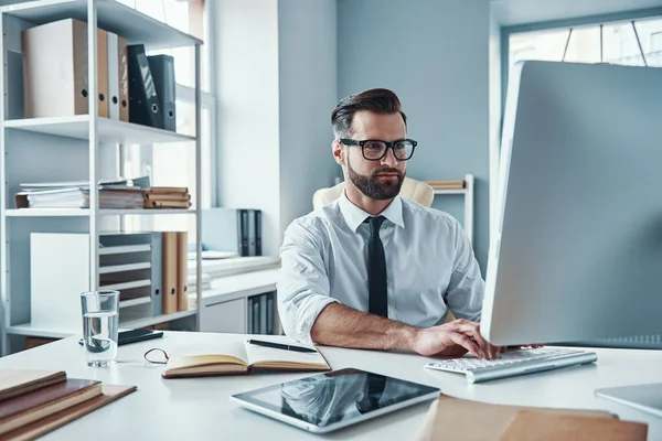 Современный молодой человек в формальной одежде, работающий по технологиям, сидя в офисе — стоковое фото