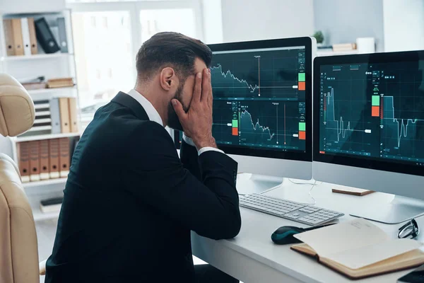 Frustrovaný mladý muž ve formálním oděvu drží hlavu v rukou, zatímco pracuje v kanceláři — Stock fotografie