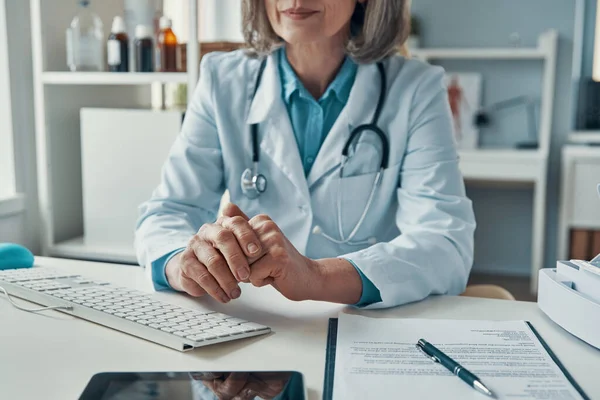 Zbliżenie w górę z Dojrzałe kobieta lekarz w biały laboratorium płaszcz trzymając ręce zaciśnięty podczas siedząc w jej biuro — Zdjęcie stockowe