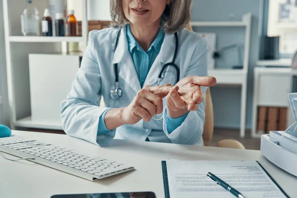 Close up de médico feminino maduro em jaleco branco dizendo algo e gesto enquanto sentado em seu escritório — Fotografia de Stock