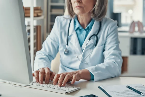 Close up of female doctor in white lab coat working using computer while sitting in her office — Stock Photo, Image