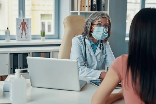 Confident female doctor in white lab coat giving a healthcare consultation to young woman while sitting in her office — Stock Photo, Image